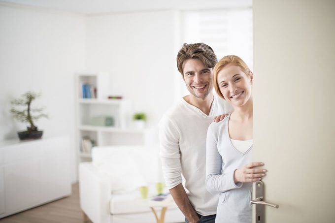 Cheerful couple inviting people to enter in home