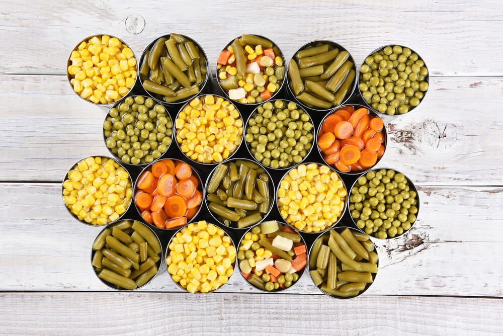 High angle shot of a group of canned vegetables on a rustic white wood table.