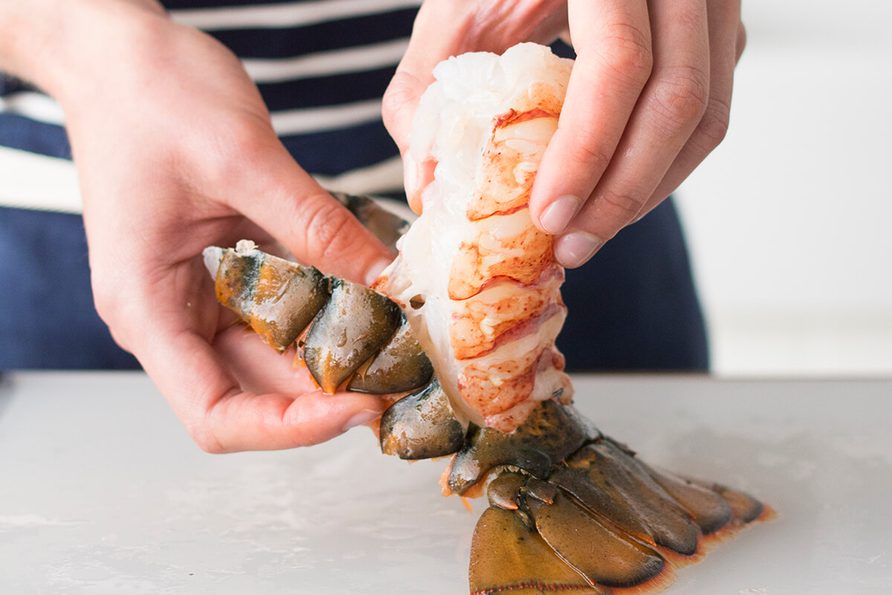 Person peeling back the shell from a lobster tail