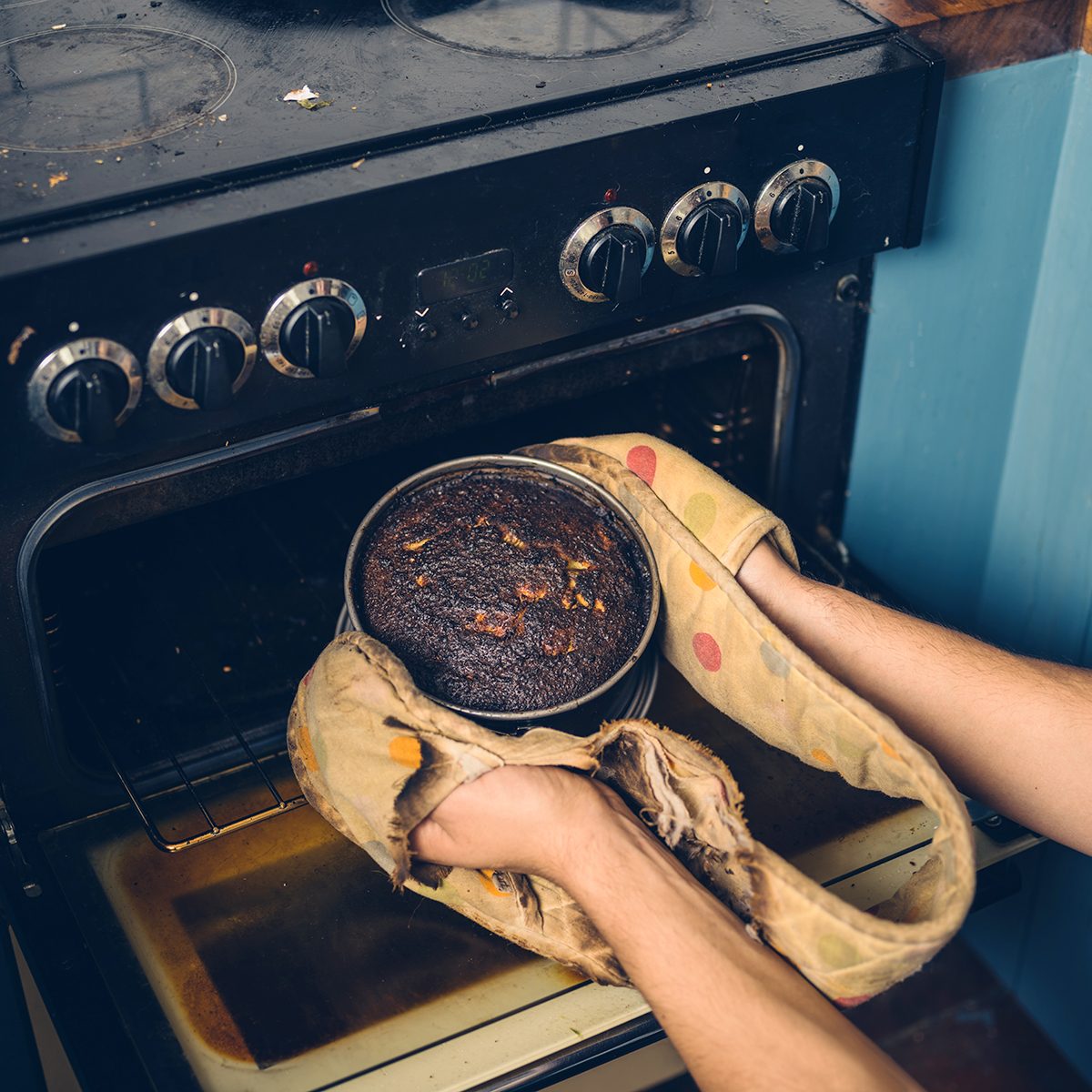 The hands of a man is removing a burnt cake from the oven