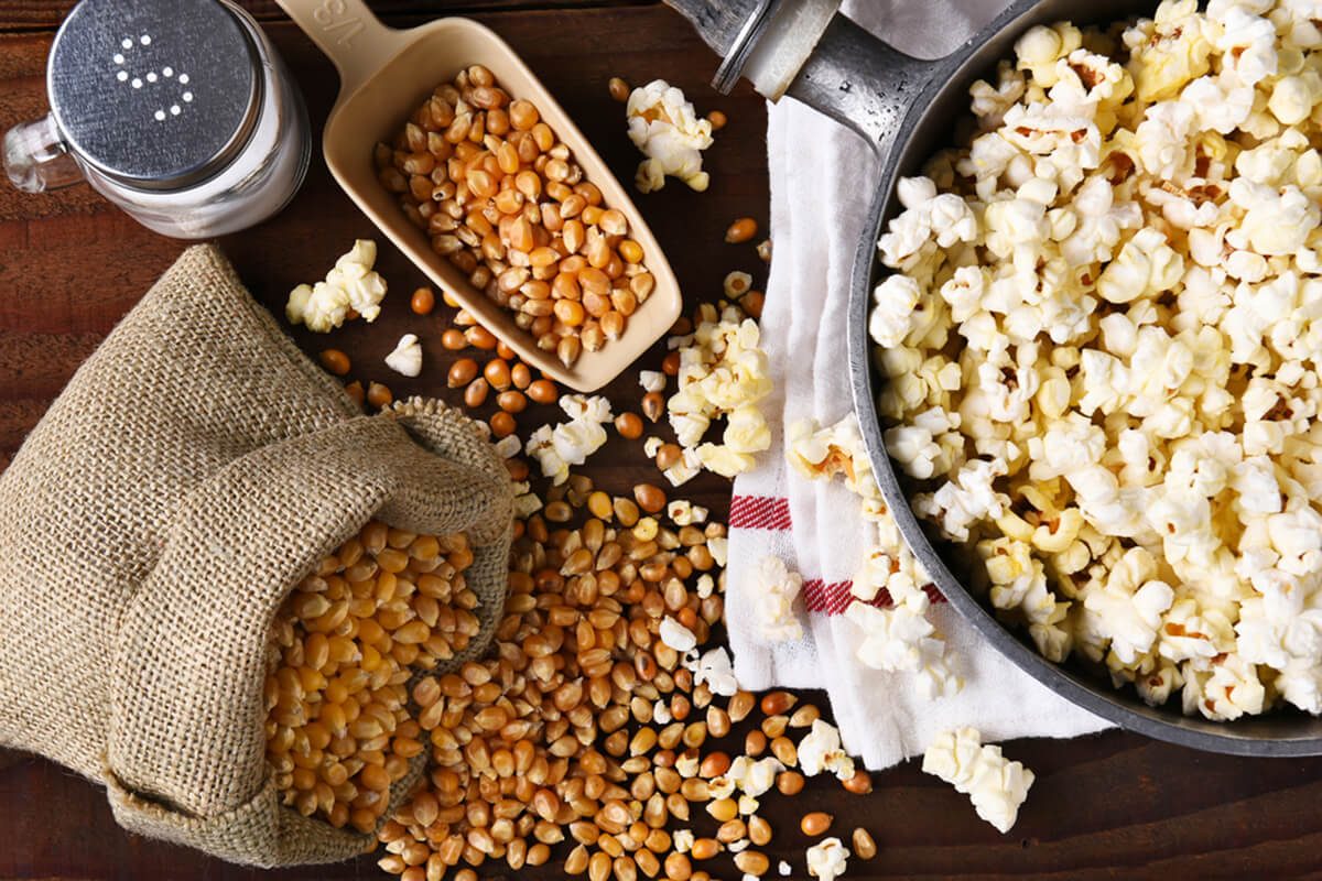 Top view of a pot full of freshly popped popcorn with salt and unpopped kernels on the side.