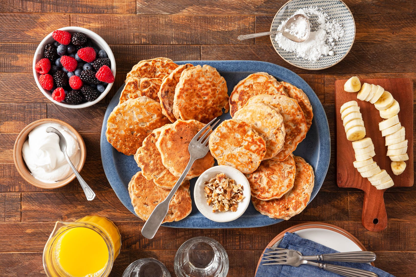 Banana Oatmeal Pancakes in a Large Blue Plate with Crushed Walnuts, Raspberries, Blueberries and Bananas on a Wooden Surface