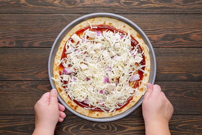 Someone Holding a Pizza Pan filled with Barbecue Chicken Pizza with hands on Wooden Surface