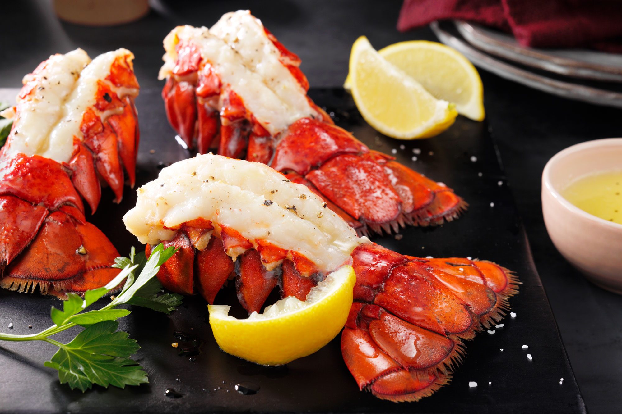 Broiled Lobster Tails with Sliced Lemons on Black Wood Cutting Board