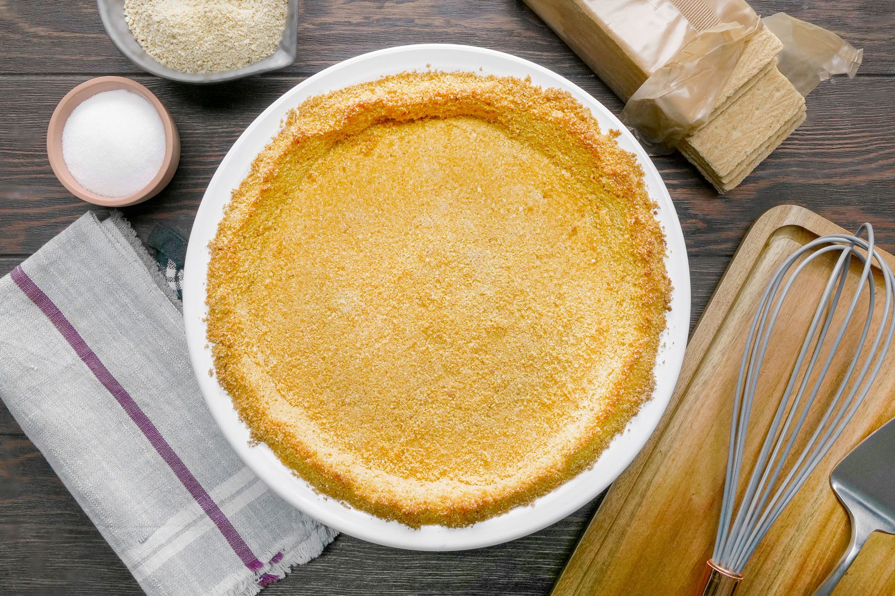 Homemade Graham Cracker Crust in White Ceramic Pie Plate on Wooden Surface