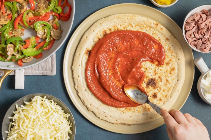 Spreading pizza sauce over the crust
