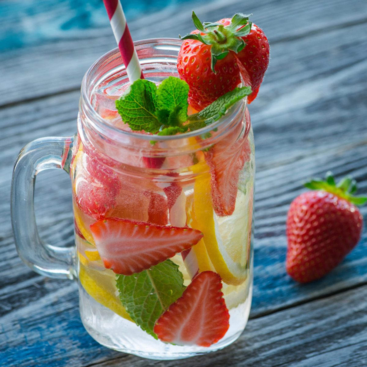 Jug with lemon and strawberry infused water on a rustic wooden table