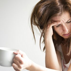 Tired and sad woman is sitting in the window seat with a cup in her hand. Depression concept