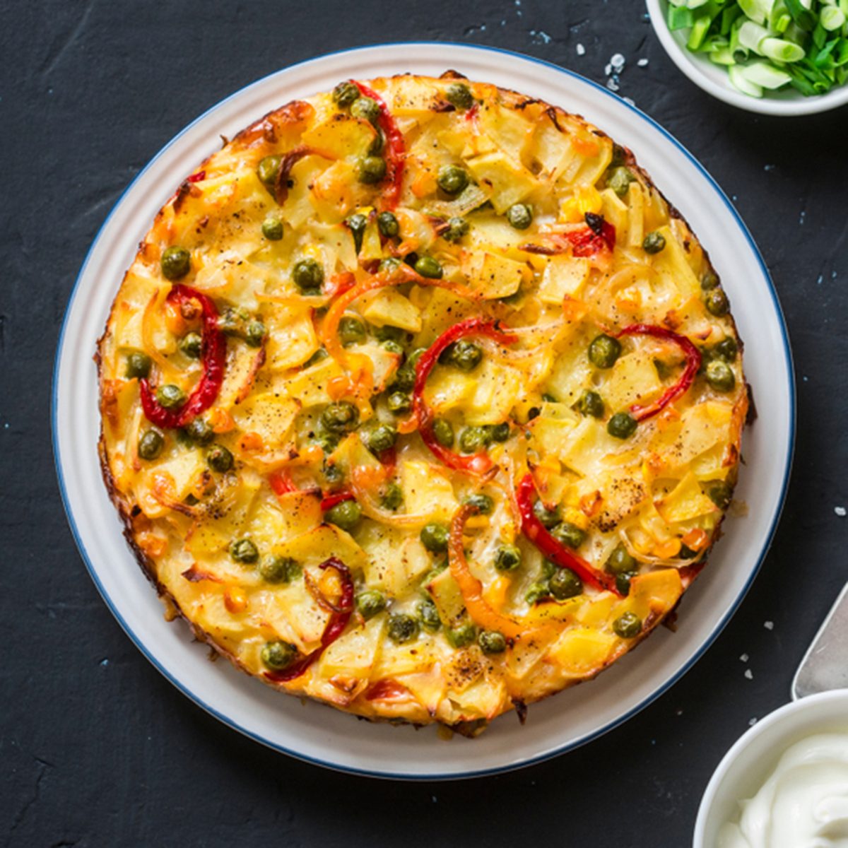 Potatoes and vegetables tortilla on a dark background, top view. Potatoes, green beans, bell peppers, green peas, cheese, eggs casserole - a delicious breakfast or snack; Shutterstock ID 1025183197; Job (TFH, TOH, RD, BNB, CWM, CM): Taste of Home