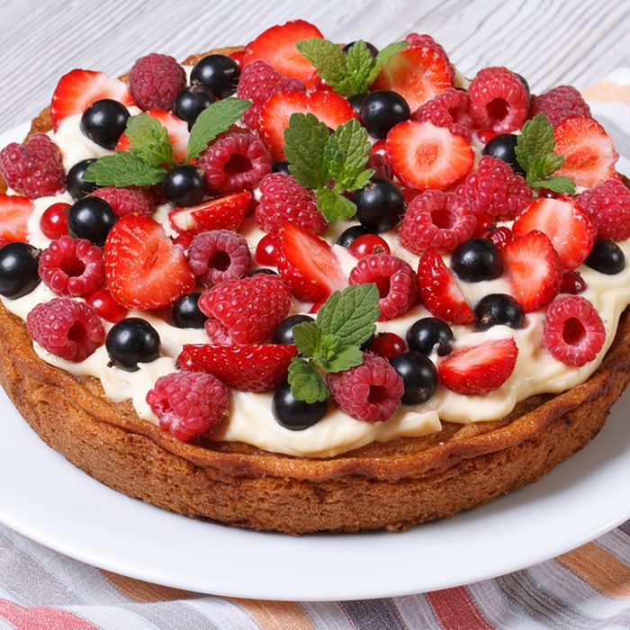 berry tart with fresh strawberries, raspberries, currants, mint and cream close up on the table