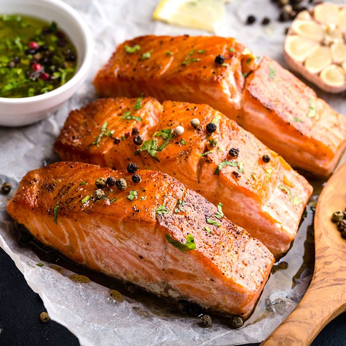 Delicious fried salmon fillet, seasonings on blue rustic concrete table. Cooked salmon steak with pepper, herbs, lemon, garlic, olive oil, spoon. Grilled fresh fish. Fish for healthy dinner. Close-up