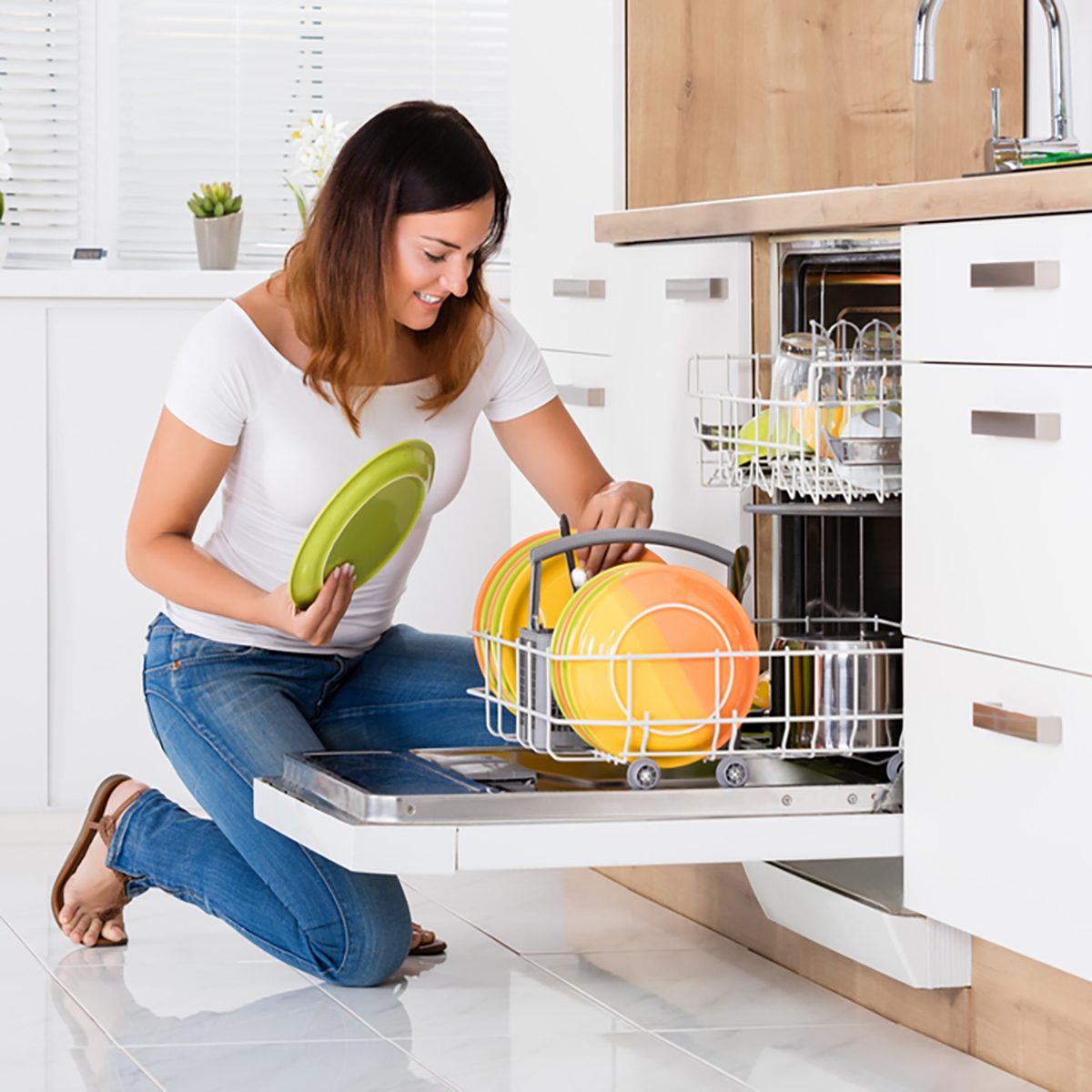 Happy Young Woman Arranging Plates In Dishwasher At Home
