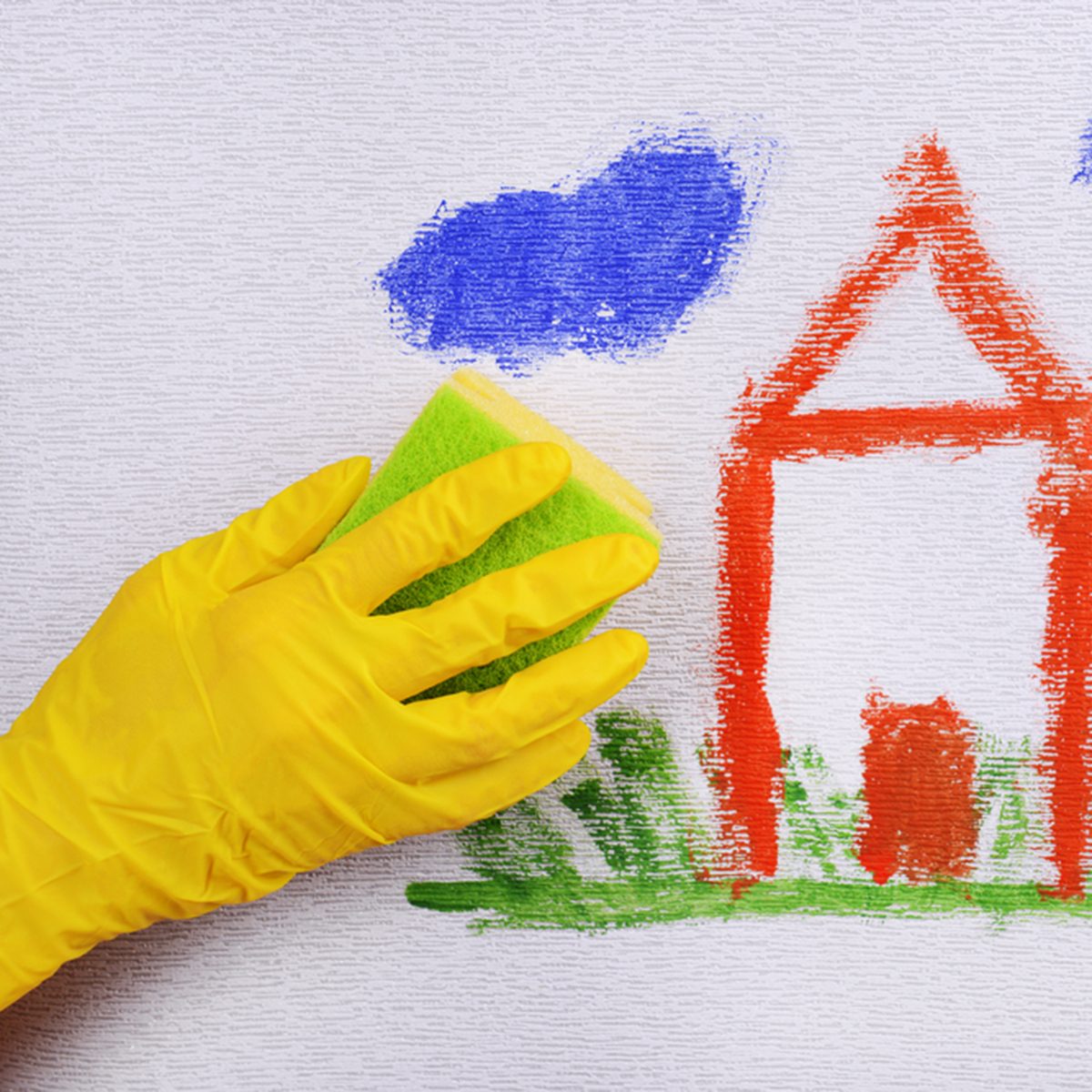 Hand in glove wiping children drawing on wallpaper