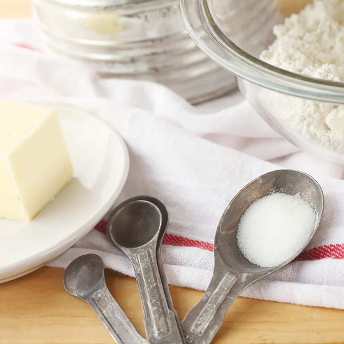 Mixing bowl with flour and butter, vintage sifter, measuring spoons and dish cloth