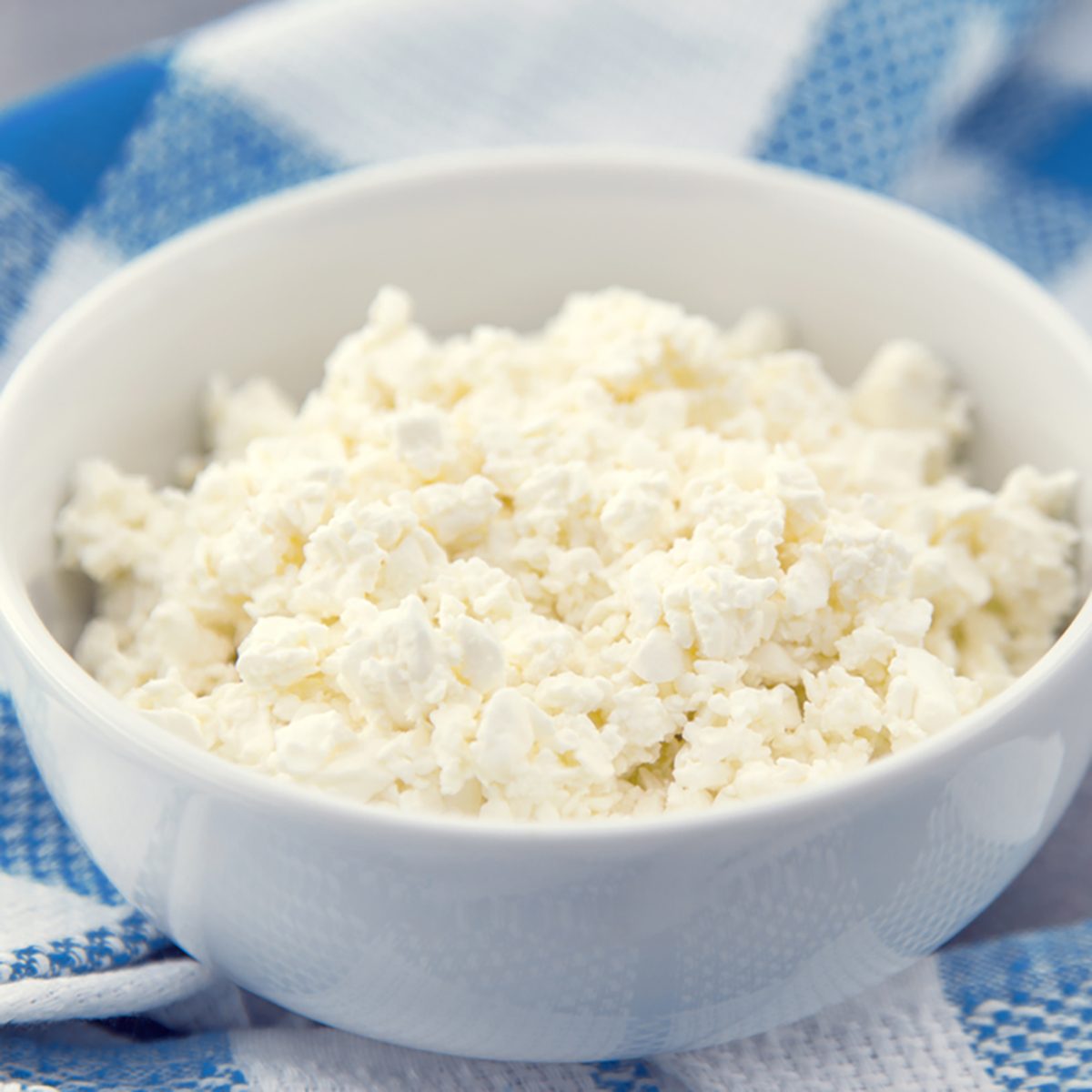 Organic cottage cheese in a white ceramic bowl on the kitchen table. Dairy products for the healthy breakfast.