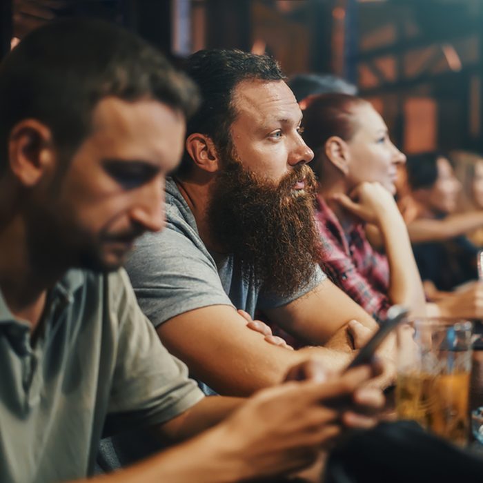 bearded man in crowded bar watching something