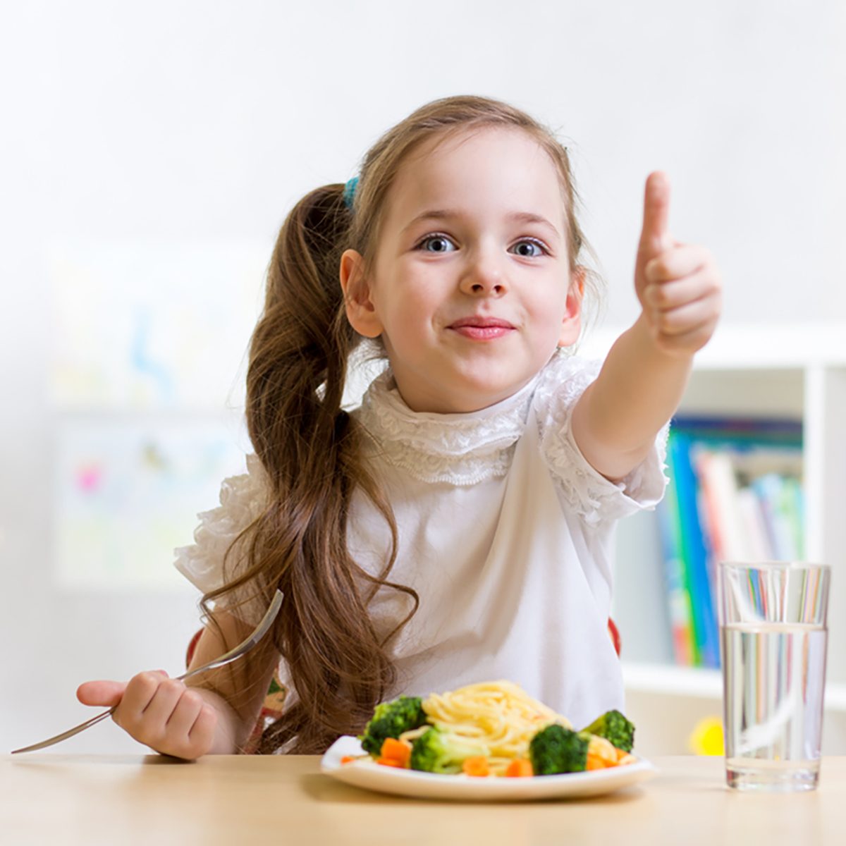 child girl eats healthy food showing thumb up at kindergarten