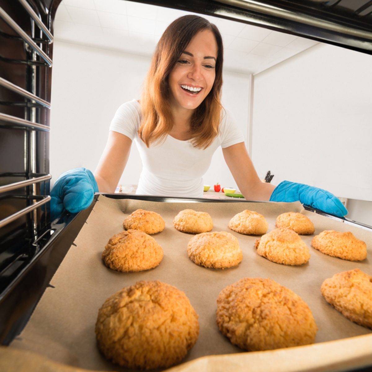 Young Happy Woman Baking Fresh Cookies In Oven At Kitchen