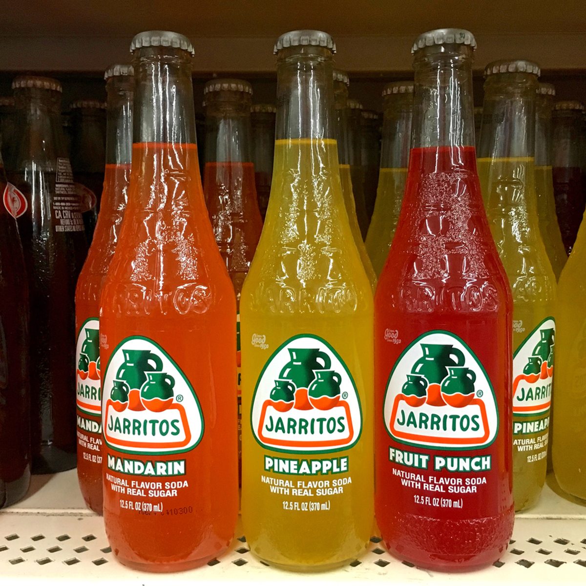 Grocery store shelf with bottles of Jarritos brand Mexican sodas.