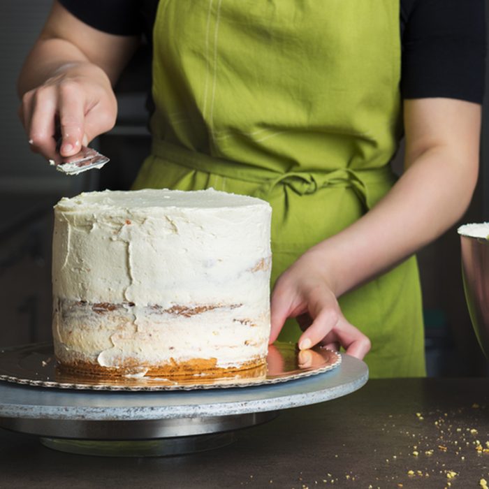 Unrecognizable woman decorating a delicious layered sponge cake with icing cream.