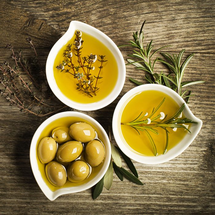 Olive oil with fresh herbs on wooden background.