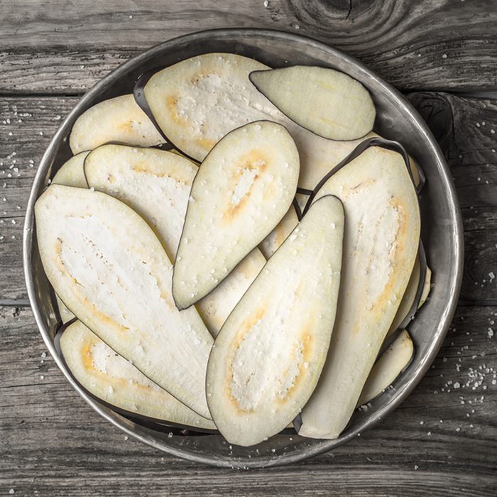 Sliced eggplants with salt in the metal plate on the wooden table top view