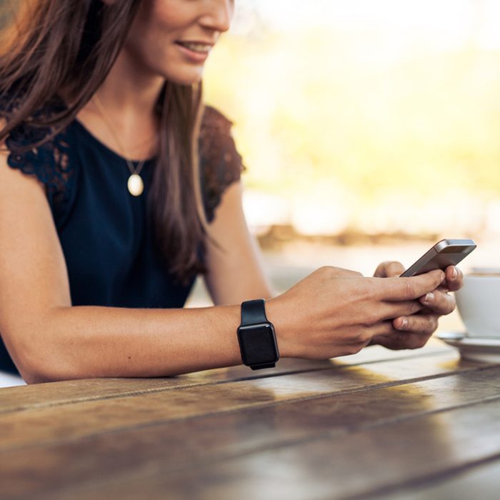 Woman typing text message on smart phone in a cafe.