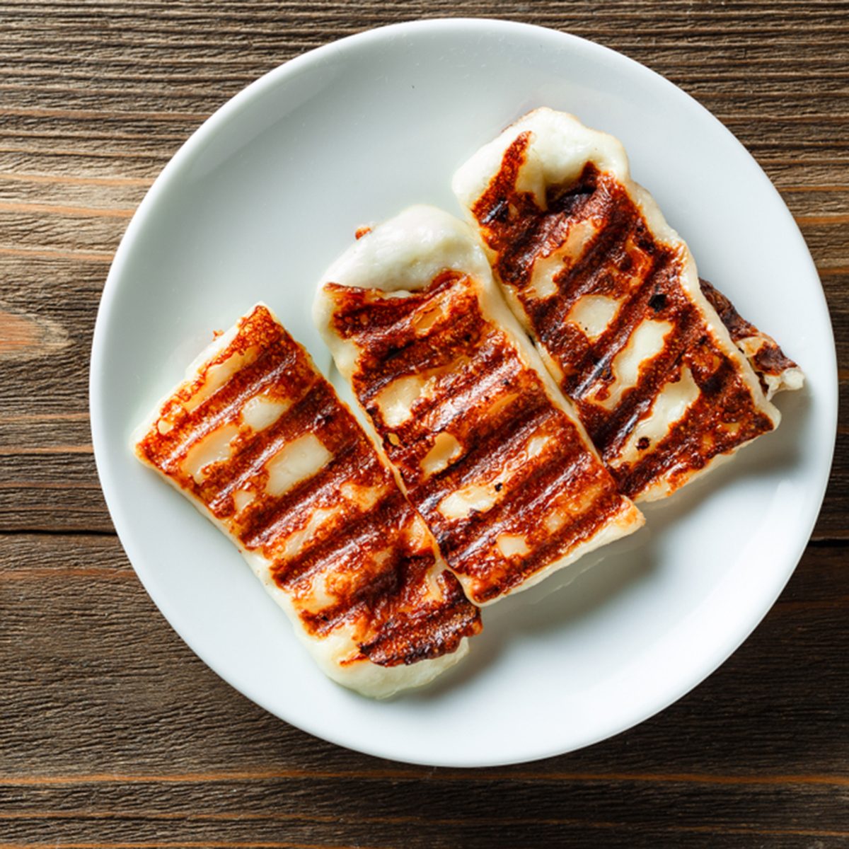 Traditional Greek Grilled Hallumi Cheese on white plate on wooden background.