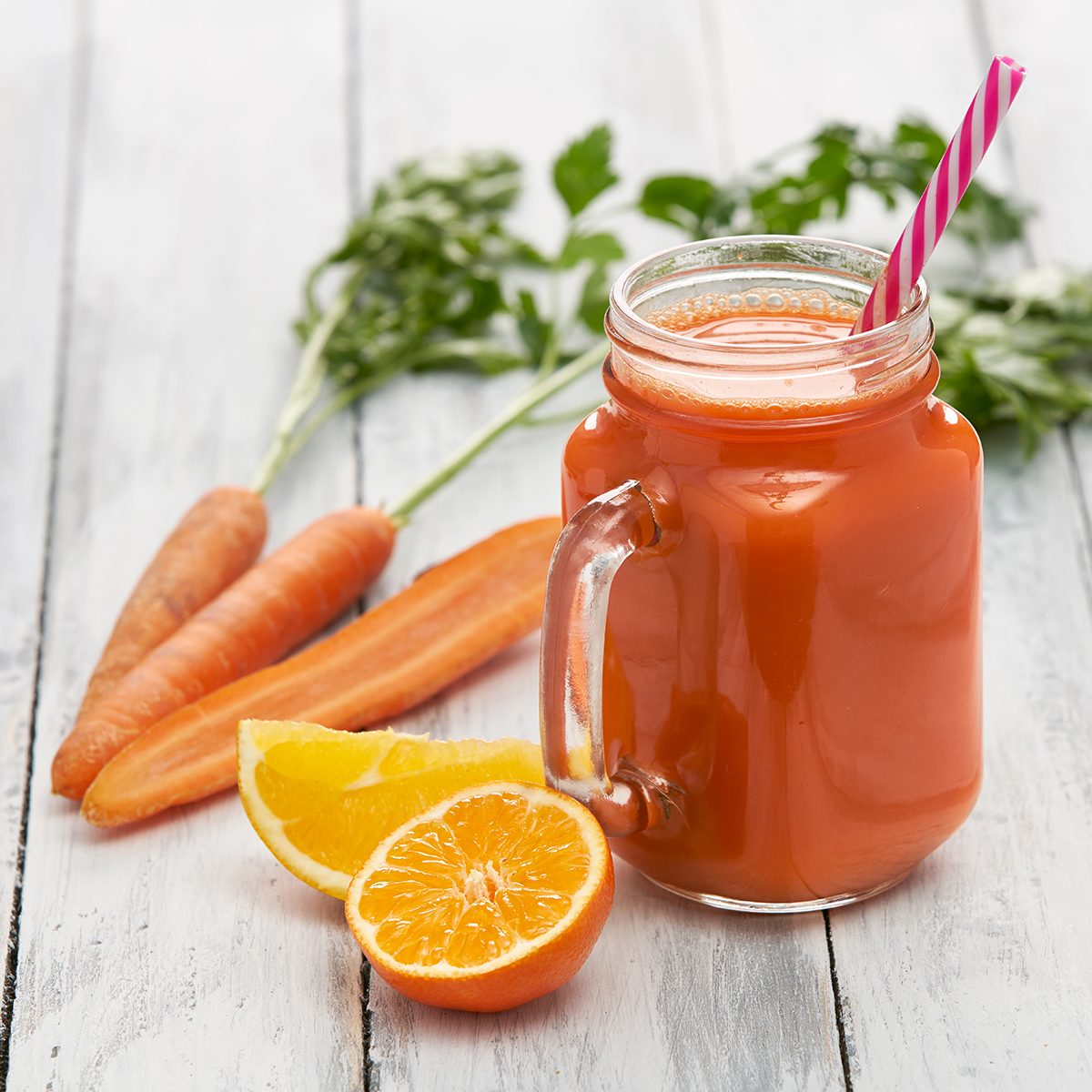 juice in a glass container surrounded by fresh vegetables and fruits on white boards