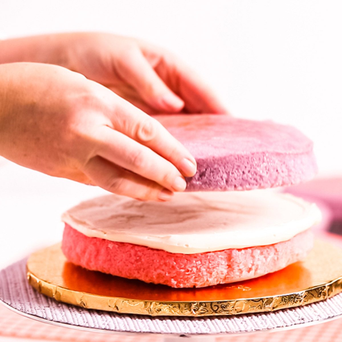 Baker assembling pink and purple cake layer to make unicorn cake for little girl