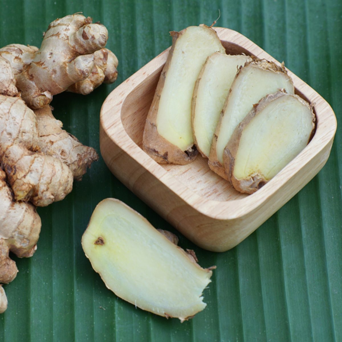 Fresh ginger root and ginger sliced on green leaf background