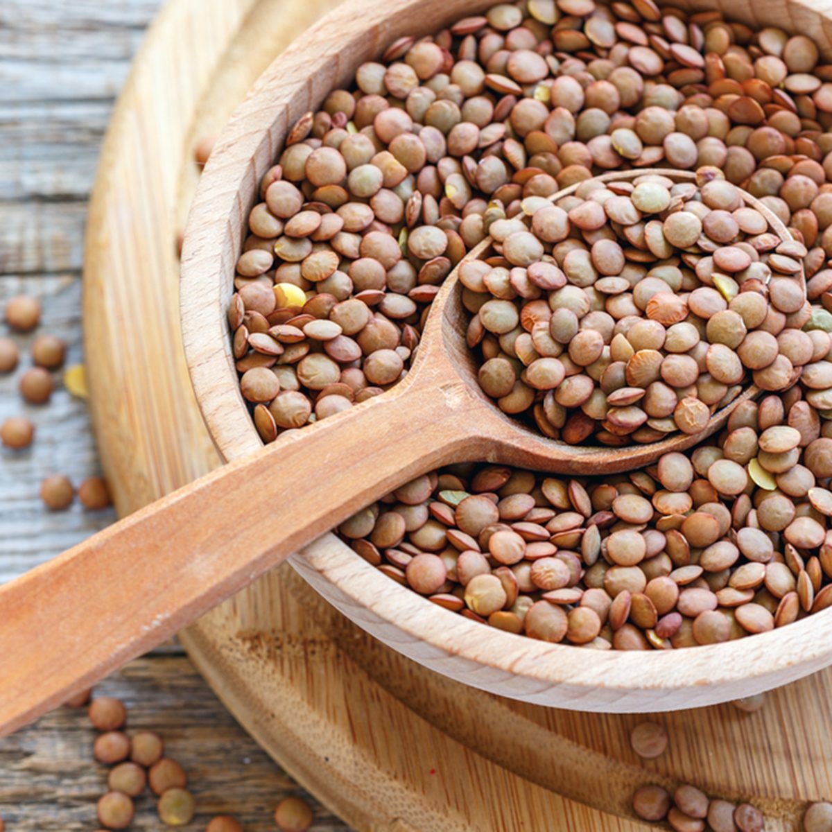 Lentils and spoon in a wooden bowl close up on an old table.