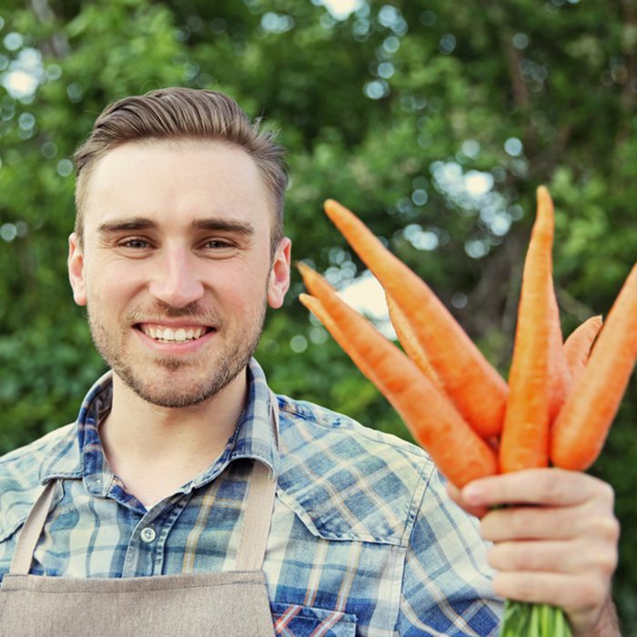 Handsome man with carrots in green garden