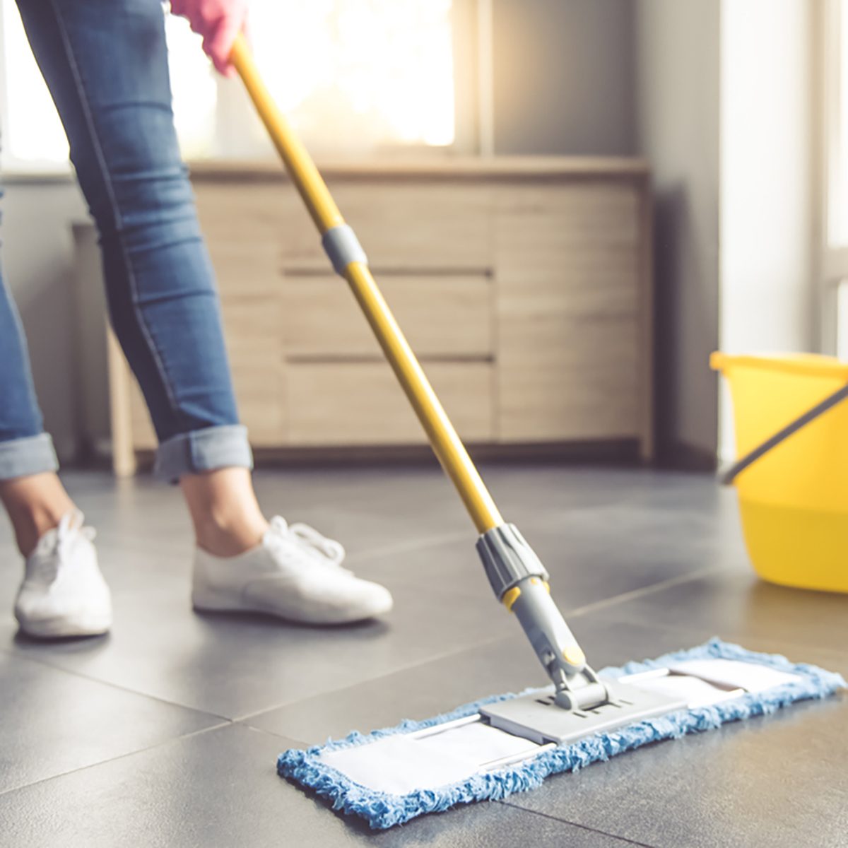 Cropped image of beautiful young woman in protective gloves using a flat wet-mop while cleaning floor in the house;