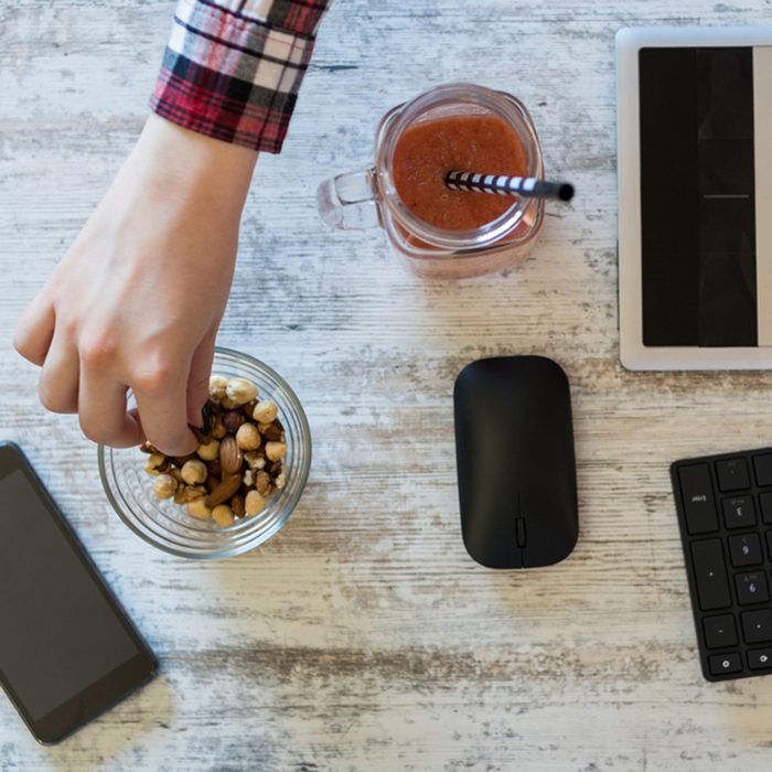 Closeup shot from above of a young businesswoman sitting at her desk and using graphic board while having a healthy snack.