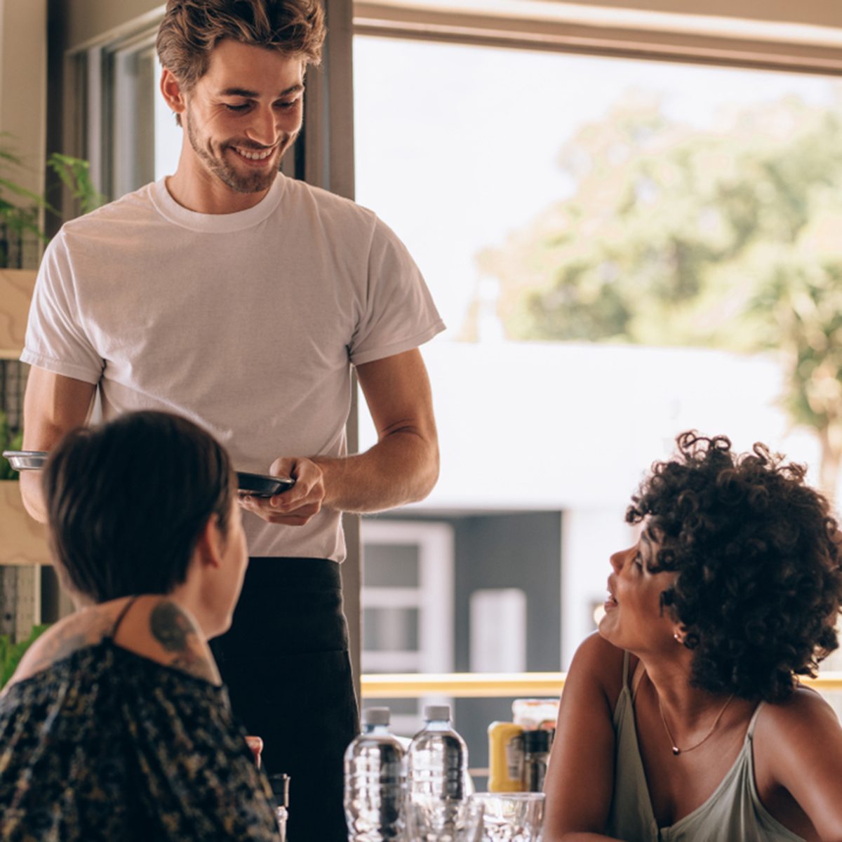 Young woman with a friend ordering to waiter at cafe.