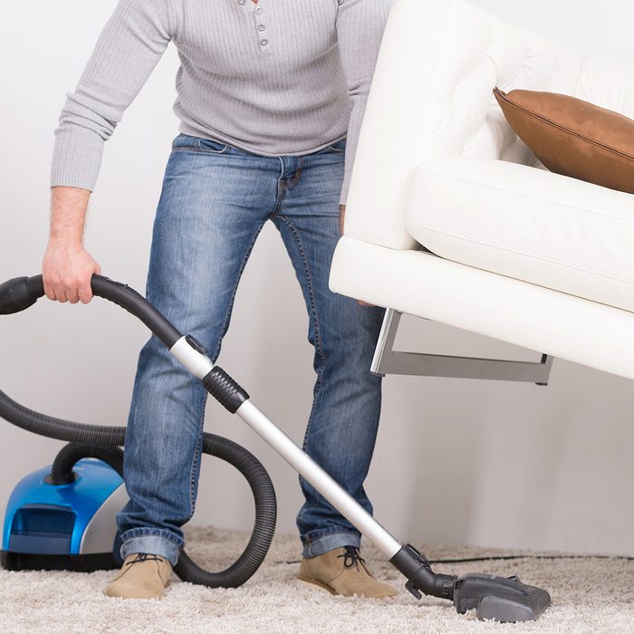 man does house work with vacuum cleaner. Men lifted sofa in living room, vacuum cleaning. ; Shutterstock ID 216002761; Job (TFH, TOH, RD, BNB, CWM, CM): TOH