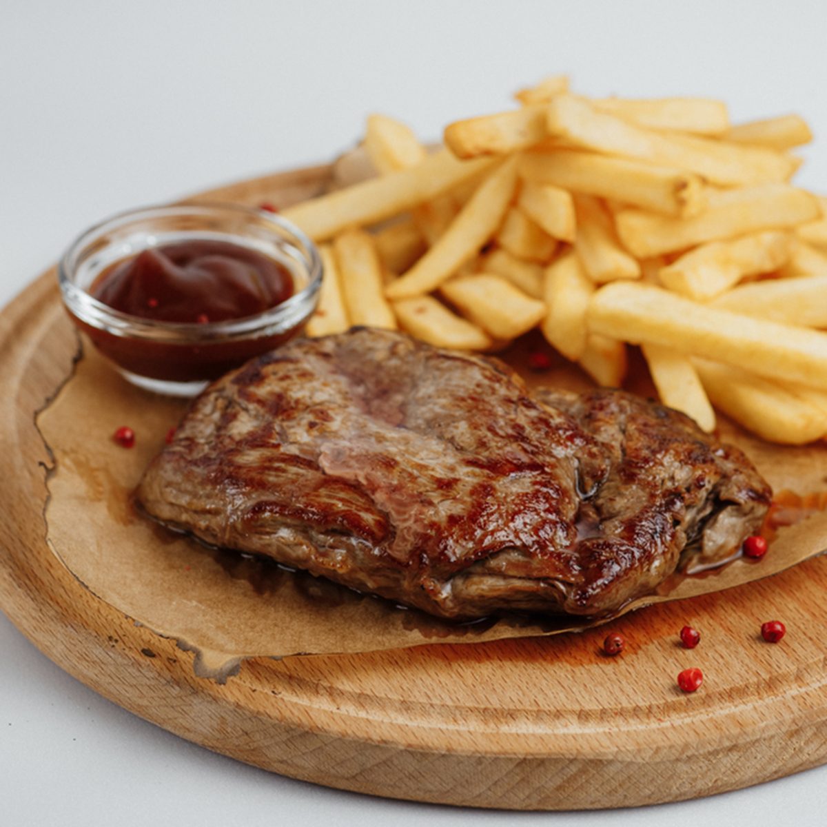 Steak with fries and sauce on a wooden tray on a white background