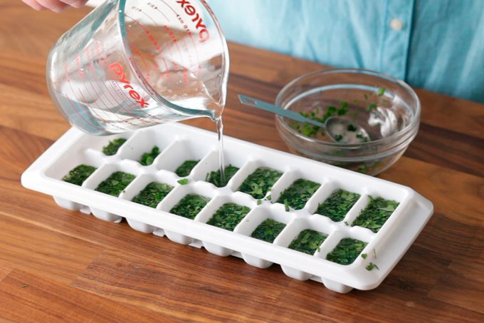 Pouring water in ice tray with herbs