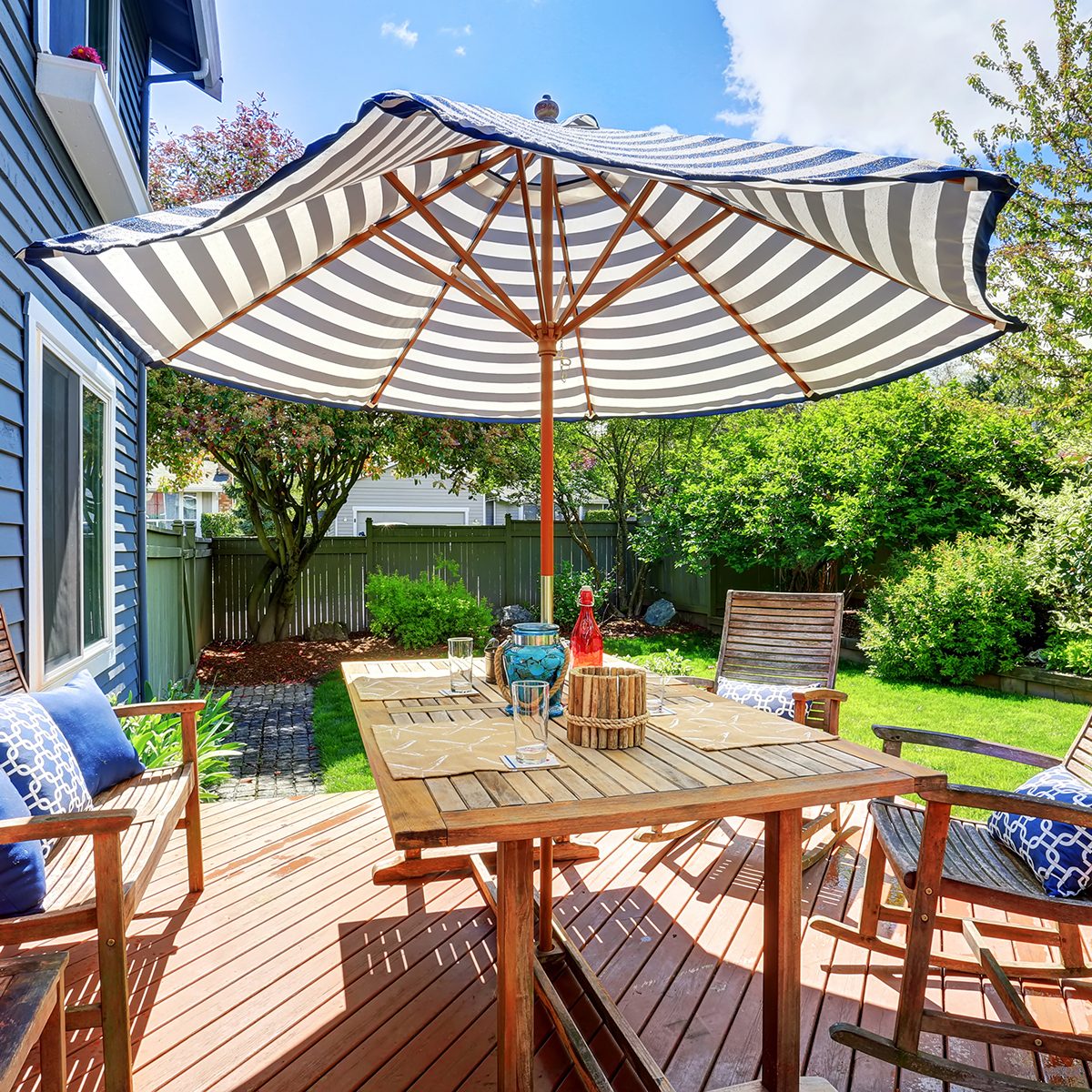 Wooden walkout deck in the backyard garden of blue siding house.
