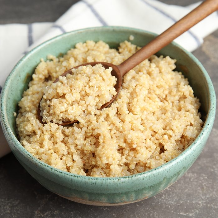 Composition with cooked quinoa in bowl and wooden spoon on table