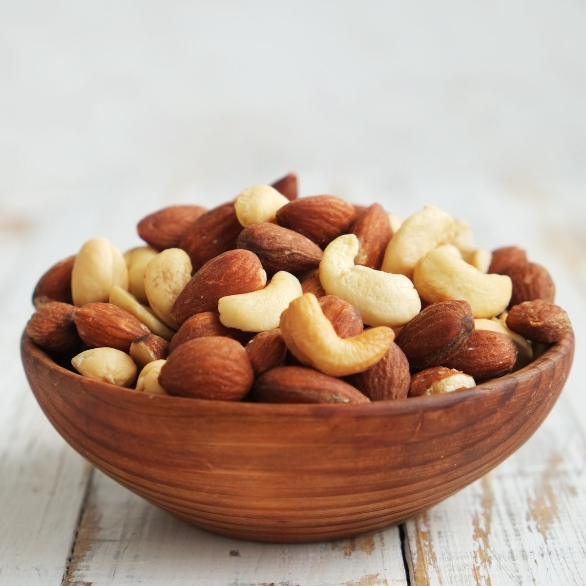 Mixed nuts in a bowl on a white wooden background.