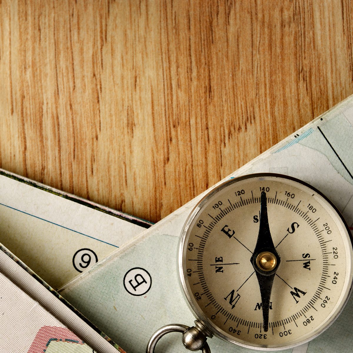 Close up Vintage Compass Instrument on Top of a Wooden Table with Folded Maps