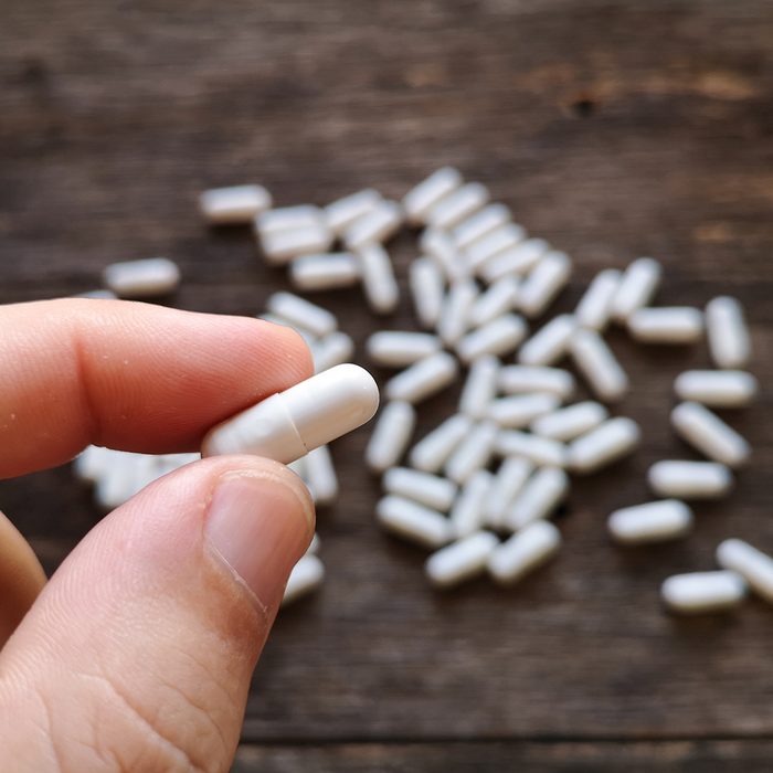 Hand holding capsules pills white on wooden background.