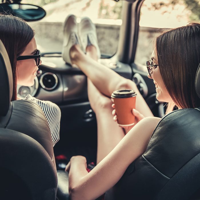 Back view of beautiful girls talking and smiling while traveling by car.