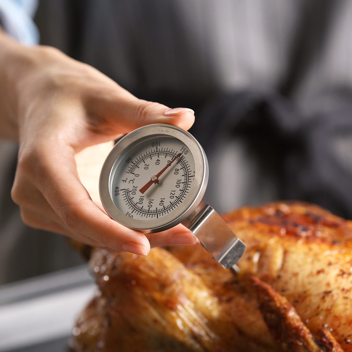 Young woman measuring temperature of whole roasted turkey with meat thermometer
