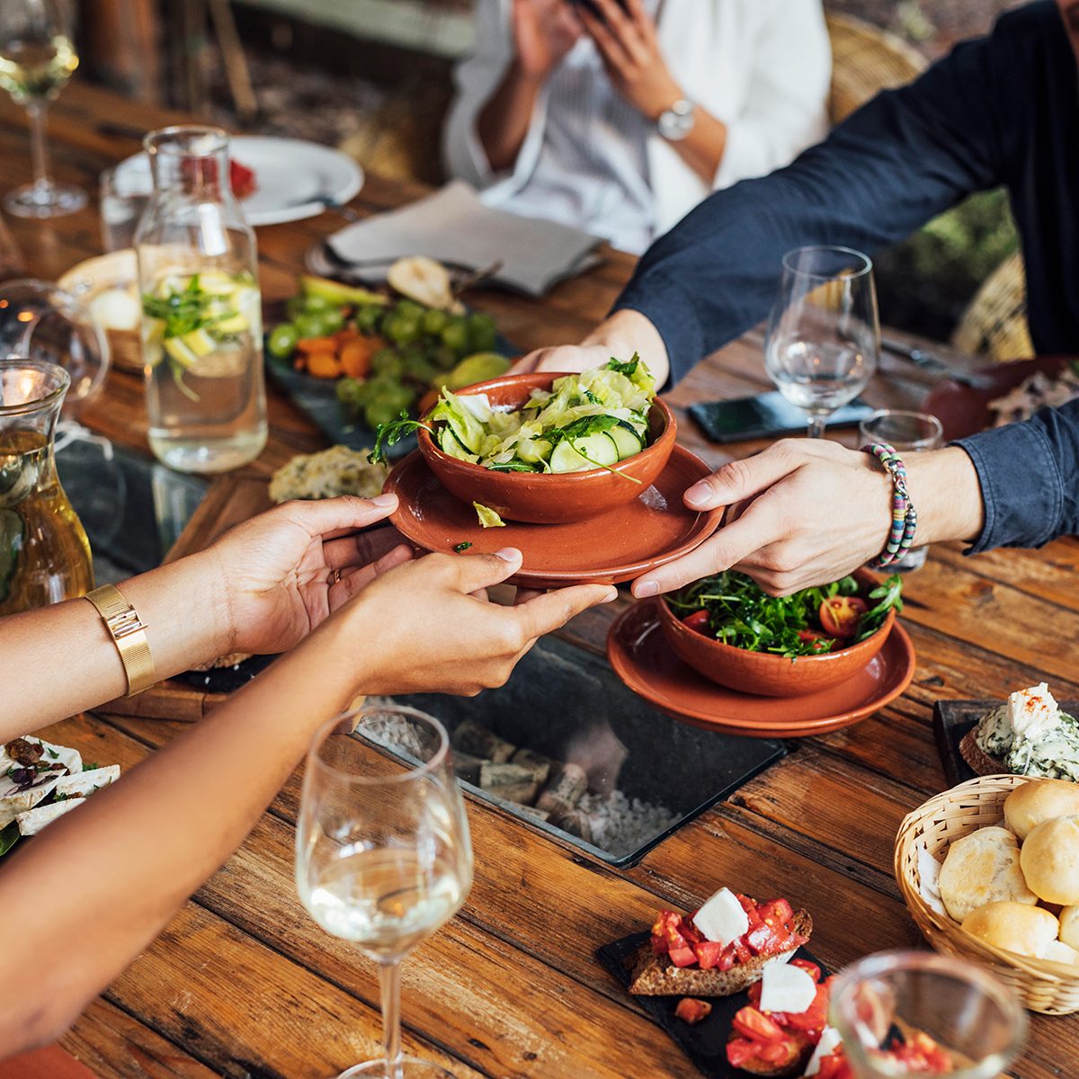 Hands of cropped unrecognisable woman and man passing salad bowl at vegetarian restaurant.