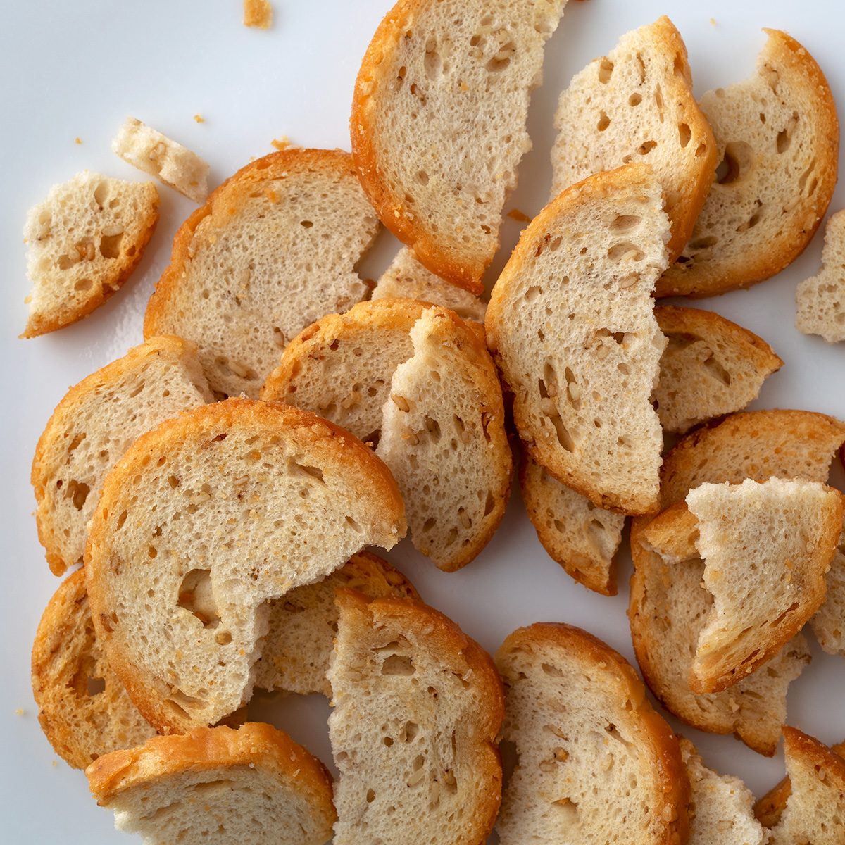 Overhead close view of broken pieces of sesame round melba toast on a white plate.; Shutterstock ID 1284342067; Job (TFH, TOH, RD, BNB, CWM, CM): TOH