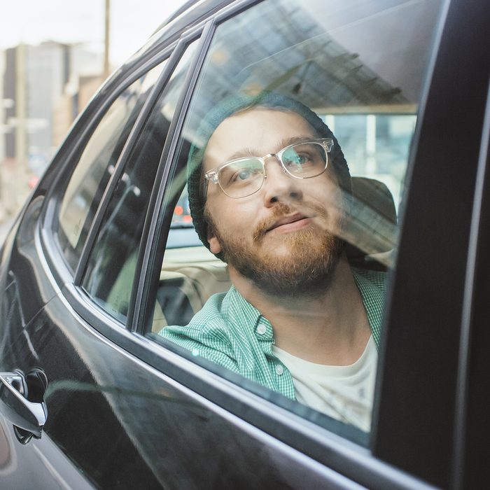 Stylish Young Man Rides on a Passenger Back Seat of a Car