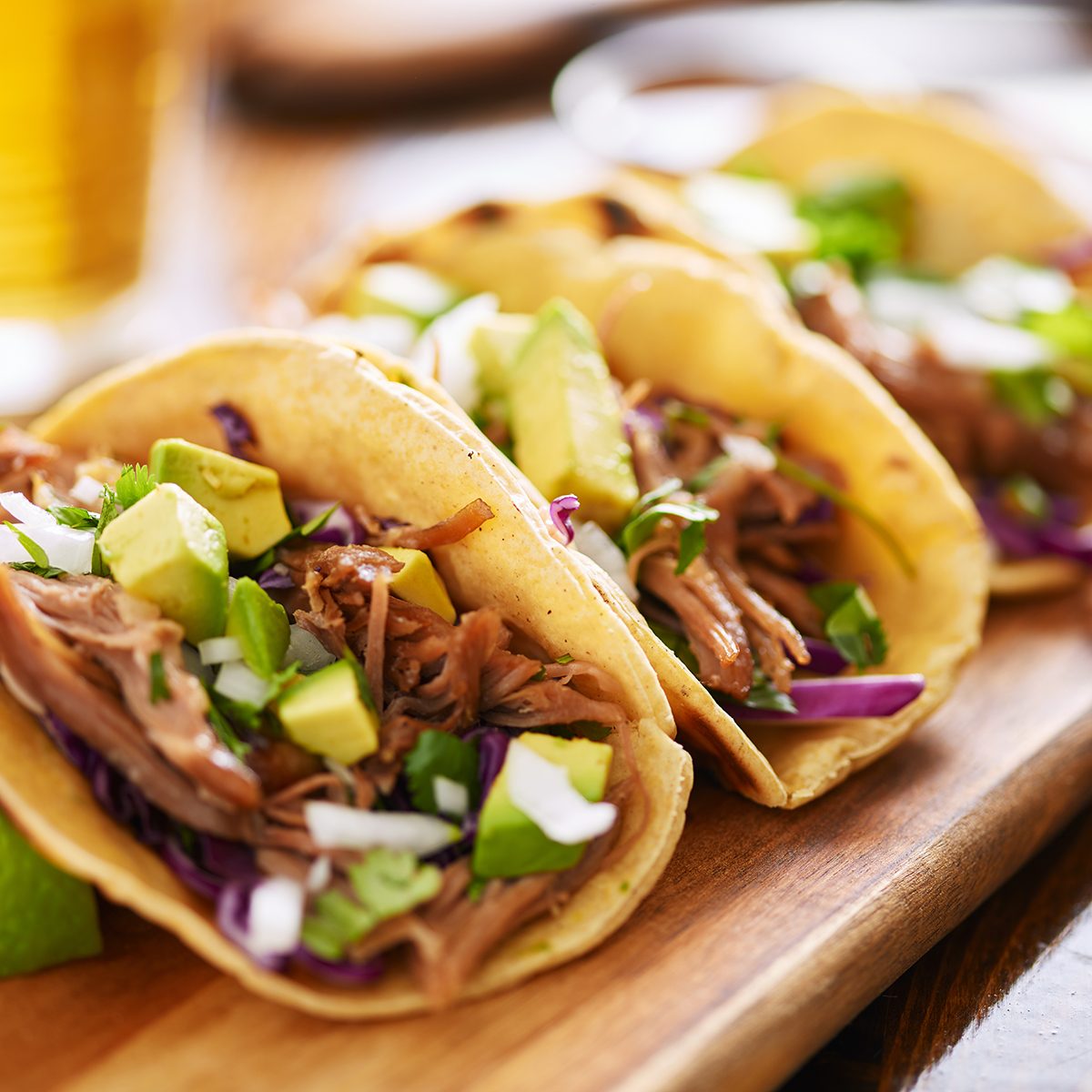 three pork carnitas street tacos in yellow corn tortilla with avocado, onion, cilantro and cabbage
